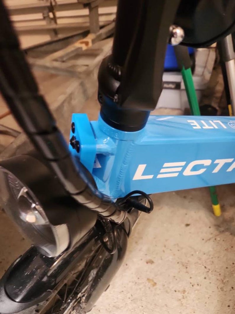 May include: A close-up of a blue electric bike with black handlebars and a black headlight. The bike has the word "LECTRA LITE" printed on the frame.