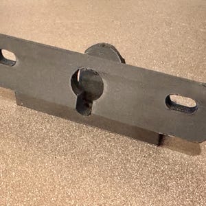 May include: A black metal bracket with a keyhole and two oval-shaped holes. The bracket is designed to be mounted to a wall or surface.