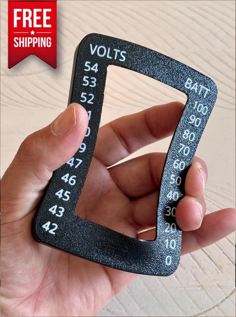 May include: Black, curved gauge with white text indicating voltage and battery levels. The gauge reads "VOLTS" and "BATT" with numerical values from 0 to 100. The gauge is held in a hand.