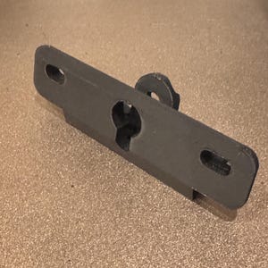 May include: A black plastic bracket with a hole in the center and two smaller holes on either side. The bracket has a small, round knob on the top.