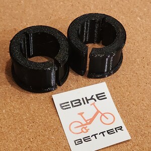 Op de afbeelding: Twee zwarte plastic ringen met een split aan &eacute;&eacute;n kant. De ringen zijn ontworpen om te worden gebruikt als kabelbinders of om items te beveiligen.