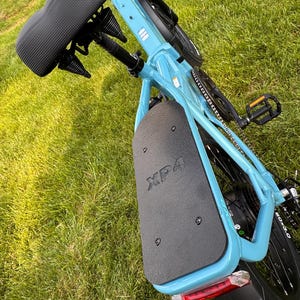 May include: A light blue electric bicycle with a black seat and black components. The rear fender has the text "XP4" printed on it. The bicycle is on a grassy surface.