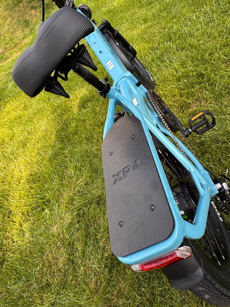 May include: A light blue electric bicycle with a black seat and black components. The rear fender has the text "XP4" printed on it. The bicycle is on a grassy surface.