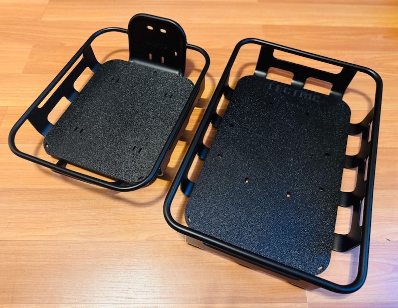 May include: Two black metal bicycle baskets. One has a back support with mounting holes. The other has the word "LECTRIC" printed on the base. Both have a rectangular shape with a textured base.