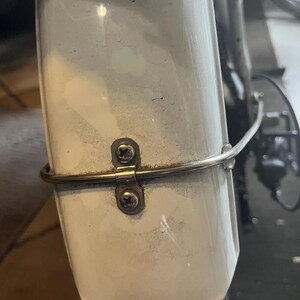 May include: White bicycle fender with a silver metal bracket attached to it with two screws. The bracket has a curved metal bar attached to it.