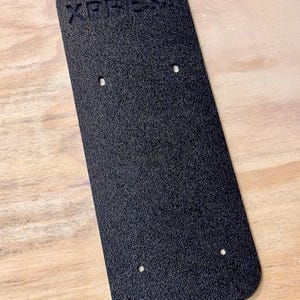 May include: Black plastic plate with the word "XPRESS" embossed on the top. The plate has four holes drilled into it.