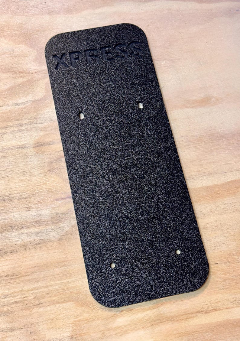 May include: Black plastic plate with the word "XPRESS" embossed on the top. The plate has four holes drilled into it.