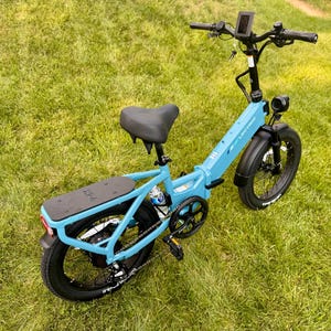 May include: A light blue Lectric XP 2.0 electric bike with black tires and a black seat is parked on a grassy lawn. The bike has a rear cargo rack, a digital display, and a headlight. The bike's frame is a vibrant blue.