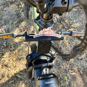 May include: An overhead view of an electric bicycle, showcasing the handlebars, front suspension, and headlight. The handlebars have orange reflectors and a sticker that says "eBikebetter". The headlight has the word "Lectric" printed on it.