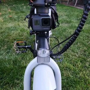 May include: A white electric bicycle with a black handlebar, a black camera mounted on the front, and a black light on the front.
