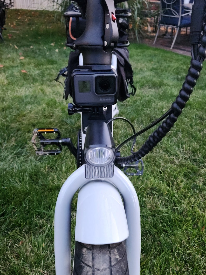 May include: A white electric bicycle with a black handlebar, a black camera mounted on the front, and a black light on the front.