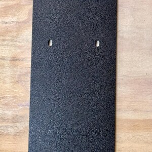 May include: Black rectangular plate with the word "XPRESS" embossed in the top centre. The plate has a textured surface and four small holes.