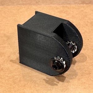 May include: A black, 3D-printed bracket with a textured surface. The bracket has a rectangular base and a curved section with a bolt and washer. The hardware is silver and black.