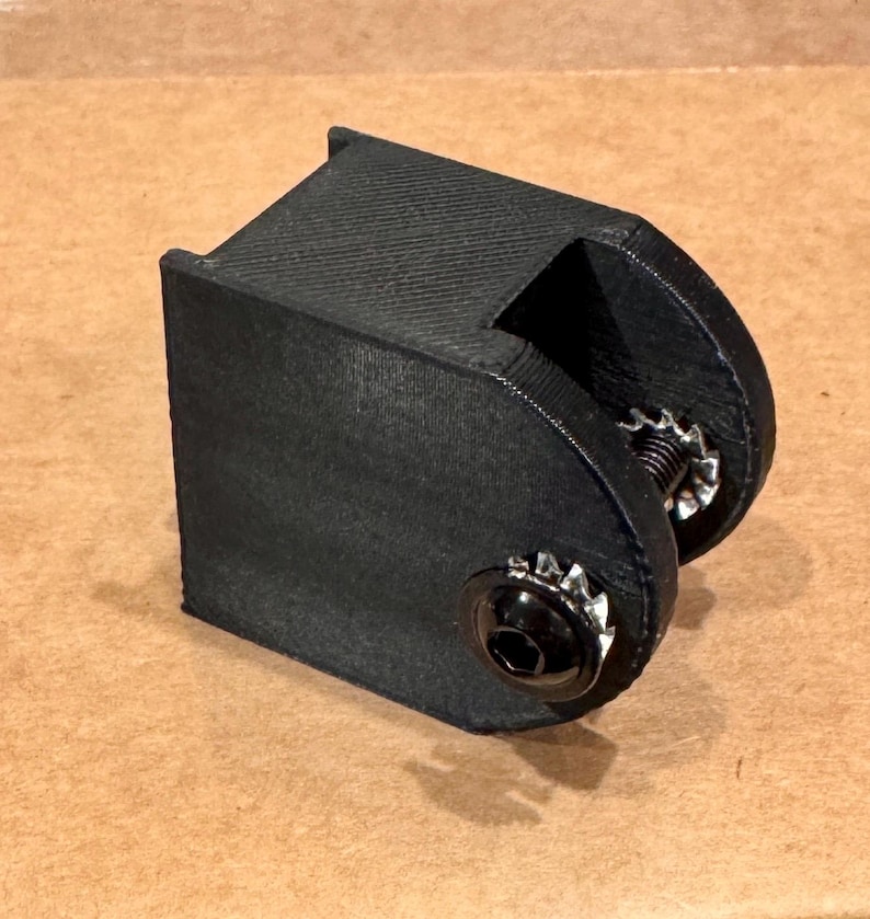 May include: A black, 3D-printed bracket with a textured surface. The bracket has a rectangular base and a curved section with a bolt and washer. The hardware is silver and black.