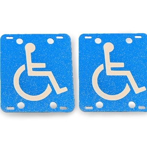 May include: Two blue square signs with white wheelchair accessibility symbols. The signs have a textured surface.