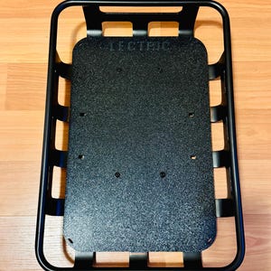 May include: Black metal cargo basket with a textured base. The word "LECTRIC" is printed on the base. The basket has a rectangular shape with rounded corners and a grid-like side design.
