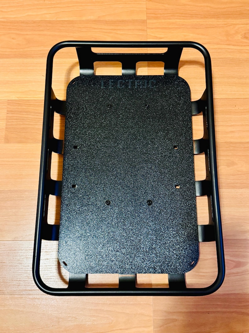 May include: Black metal cargo basket with a textured base. The word "LECTRIC" is printed on the base. The basket has a rectangular shape with rounded corners and a grid-like side design.