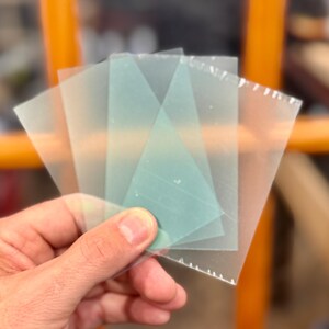 May include: Four translucent sheets of plastic, two are clear and two are a light green color. The sheets are stacked on top of each other.
