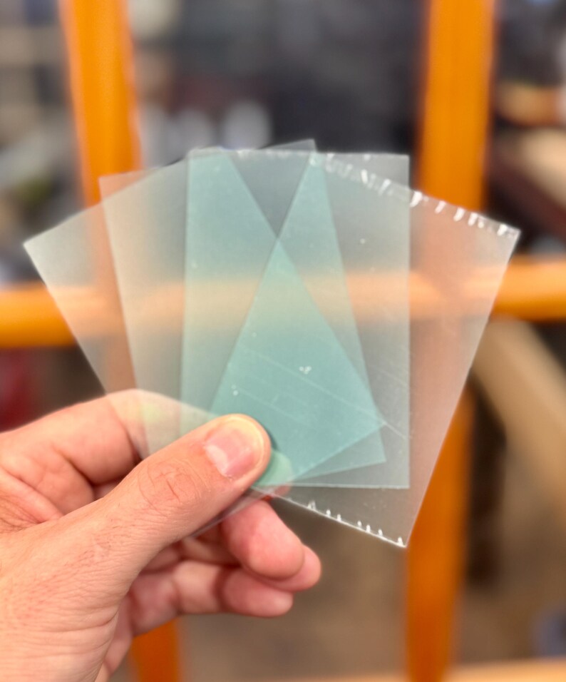 May include: Four translucent sheets of plastic, two are clear and two are a light green color. The sheets are stacked on top of each other.