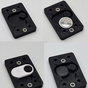 May include: A black rectangular holder with rounded edges, featuring a circular indentation and several screw holes. The word "TOP" is printed on the top. The holder is designed to accommodate various tracking devices, including an Apple AirTag, a Tile, and a SmartTag.