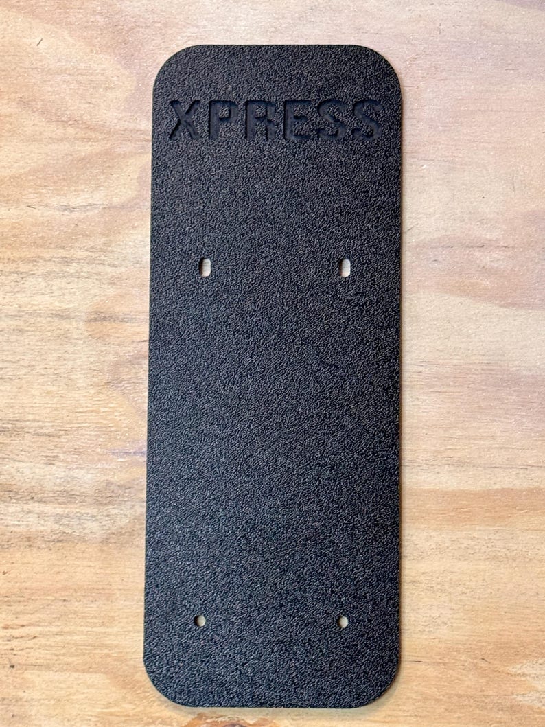 May include: Black rectangular plate with the word "XPRESS" embossed on the top. The plate has four holes drilled into it.