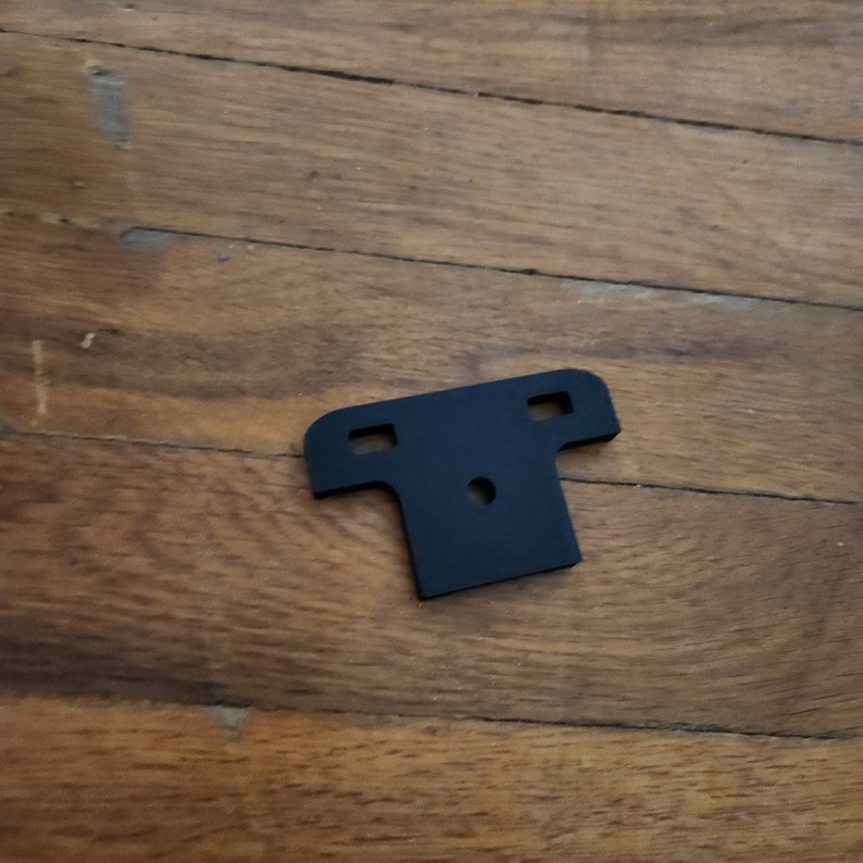 May include: A black plastic T-shaped bracket with two holes on each side and a single hole in the center.