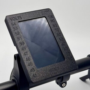 May include: Black electric bike display with a digital screen showing voltage and speed. The display is mounted on a black handlebar.