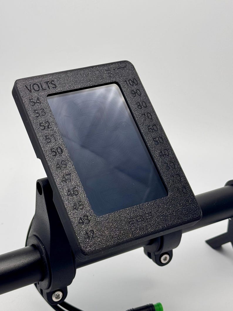 May include: Black electric bike display with a digital screen showing voltage and speed. The display is mounted on a black handlebar.