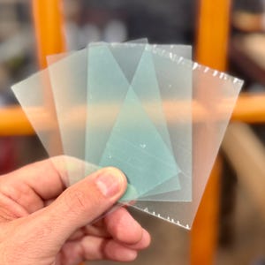 May include: Four translucent sheets of plastic, two are clear and two are a light green color. The sheets are stacked on top of each other.
