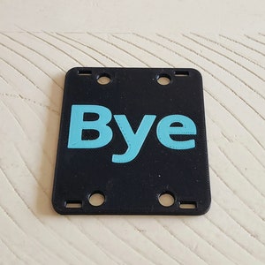 May include: Black plastic sign with four holes and the word "Bye" in light blue.