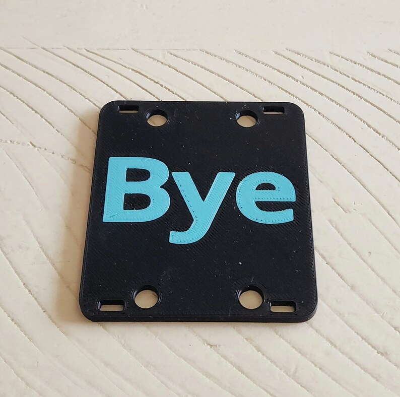 May include: Black plastic sign with four holes and the word "Bye" in light blue.