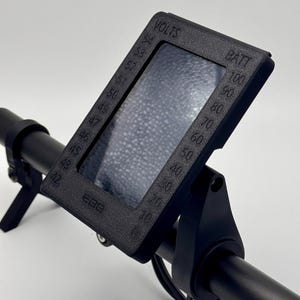 May include: Black handlebar mount with a digital display showing voltage and battery percentage. The display has a clear plastic screen and is labeled "VOLTS" and "BATT".