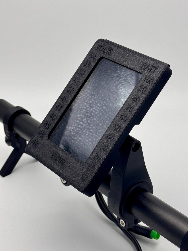 May include: Black handlebar mount with a digital display showing voltage and battery percentage. The display has a clear plastic screen and is labeled "VOLTS" and "BATT".