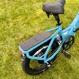 May include: A light blue electric bicycle with a black seat and a black rear fender. The bike has a black rear tire and a black platform. The text "XP" is visible on the platform.