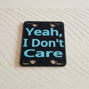 May include: Black plastic sign with the text "Yeah, I Don't Care" in light blue.
