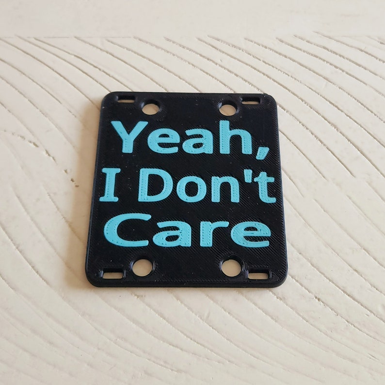 May include: Black plastic sign with the text "Yeah, I Don't Care" in light blue.