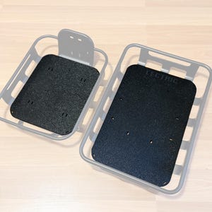 May include: Two grey rectangular baskets with black inserts. One basket has a handle. The word "LECTRIC" is visible on one of the black inserts. The baskets are on a light wood surface.