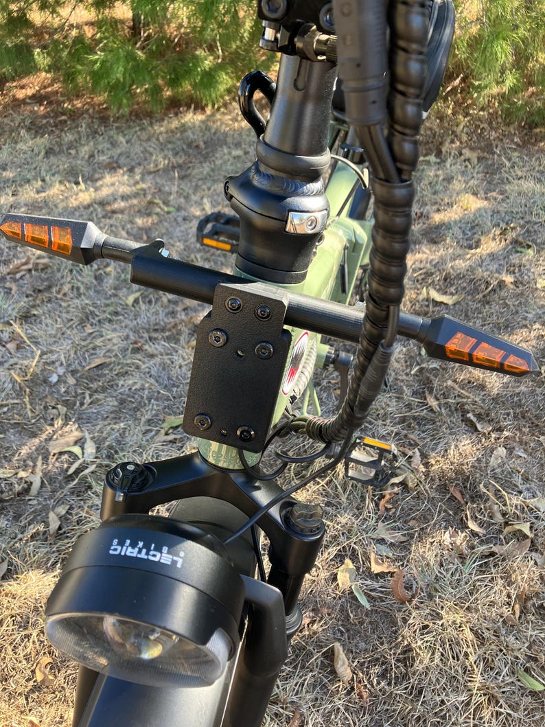 May include: Close-up of an electric bicycle's handlebars, featuring a black frame and a headlight with the word "Lectric" printed on it. The handlebars have orange turn signals on each end. The bike is green.