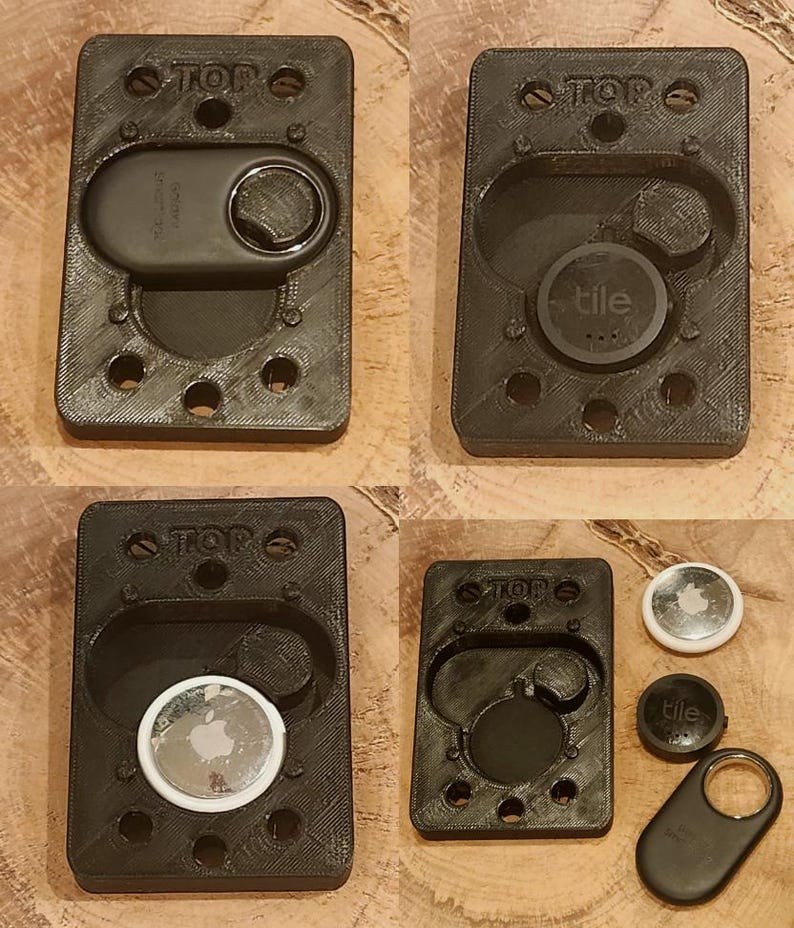 May include: Black 3D-printed holders for tracking devices. The holders are rectangular with rounded edges and feature the word "TOP" at the top. The holders are designed to fit various tracking devices, including Tile and Apple AirTag.