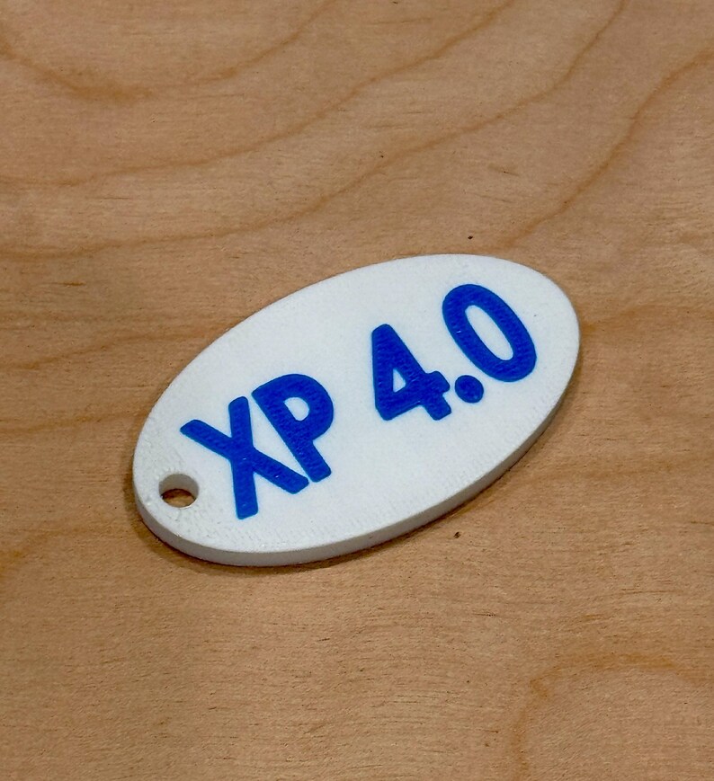 May include: White oval tag with the blue text "XP 4.0". The tag has a small hole on the left side. The tag is on a wooden surface.