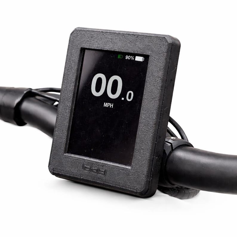May include: A black digital display showing "00.0 MPH" with a battery indicator at 90%. The display is mounted on a black handlebar. The screen is in a black rectangular frame.