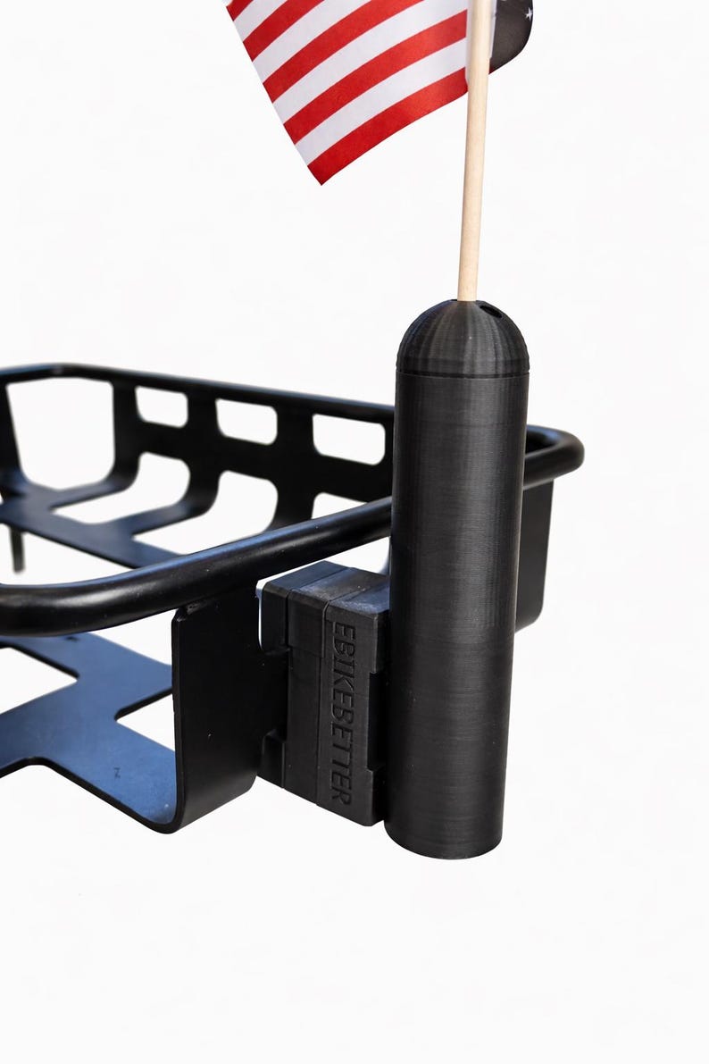 May include: Black metal bicycle basket with a flag holder. The holder has a small American flag with red and white stripes. The text "EBIKEBETTER" is visible on the mounting bracket.