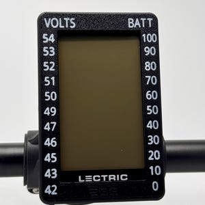 May include: A black digital display with white text indicating voltage and battery levels. The display reads "VOLTS" and "BATT" with corresponding numerical values. The brand name "LECTRIC" is visible on the display.
