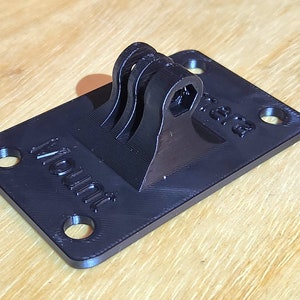 May include: A black 3D printed GoPro mount with the word "Mount" printed on the base. The mount has a swiveling arm with a hexagonal hole for attaching a camera.