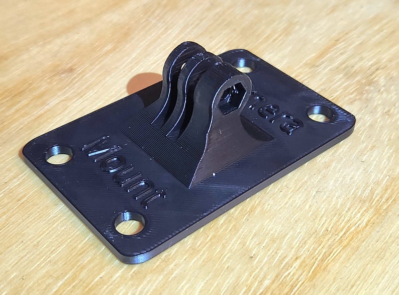 May include: A black 3D printed GoPro mount with the word "Mount" printed on the base. The mount has a swiveling arm with a hexagonal hole for attaching a camera.