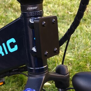May include: Close-up of a black electric bicycle with a black metal plate attached to the frame. The plate has several screws and the text "neco" is visible on the frame.