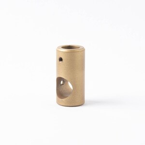 May include: A gold-colored metal cylinder with a round hole cut out of the side. The cylinder has a small hole on the top.