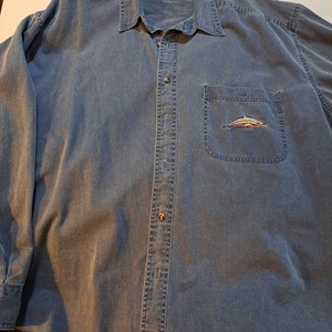 May include: A blue denim long-sleeve button-down shirt with a small embroidered dolphin on the left chest pocket.