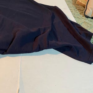 K&ouml;nnte beinhalten: Ein dunkelblaues T-Shirt mit kurzen &Auml;rmeln und Rundhalsausschnitt. Der Stoff ist glatt und blickdicht und weist nat&uuml;rliche Falten auf der Oberfl&auml;che auf. Das Kleidungsst&uuml;ck liegt flach und zeigt die Schulternaht sowie die &Auml;rmelkonstruktion.