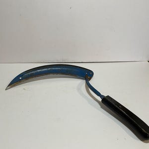 May include: A blue metal hand sickle with a black plastic handle. The sickle is curved and has a sharp blade.